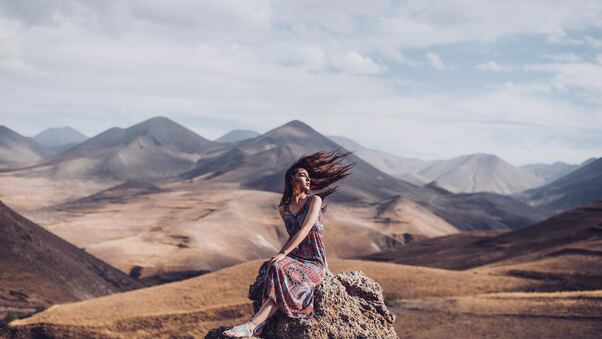 Girl Sitting On Rock Hairs In Air Wallpaper