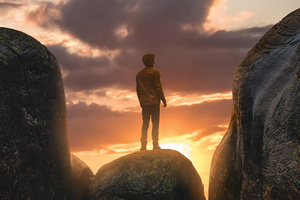 Boy Standing On A Boulder In Between Mountains