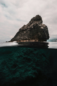 A Large Rock Sticking Out Of The Water (480x800) Resolution Wallpaper