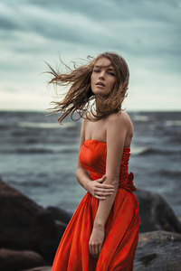 1280x2120 Girl In Orange Dress Wind Blowing At Beach Rocks 4k